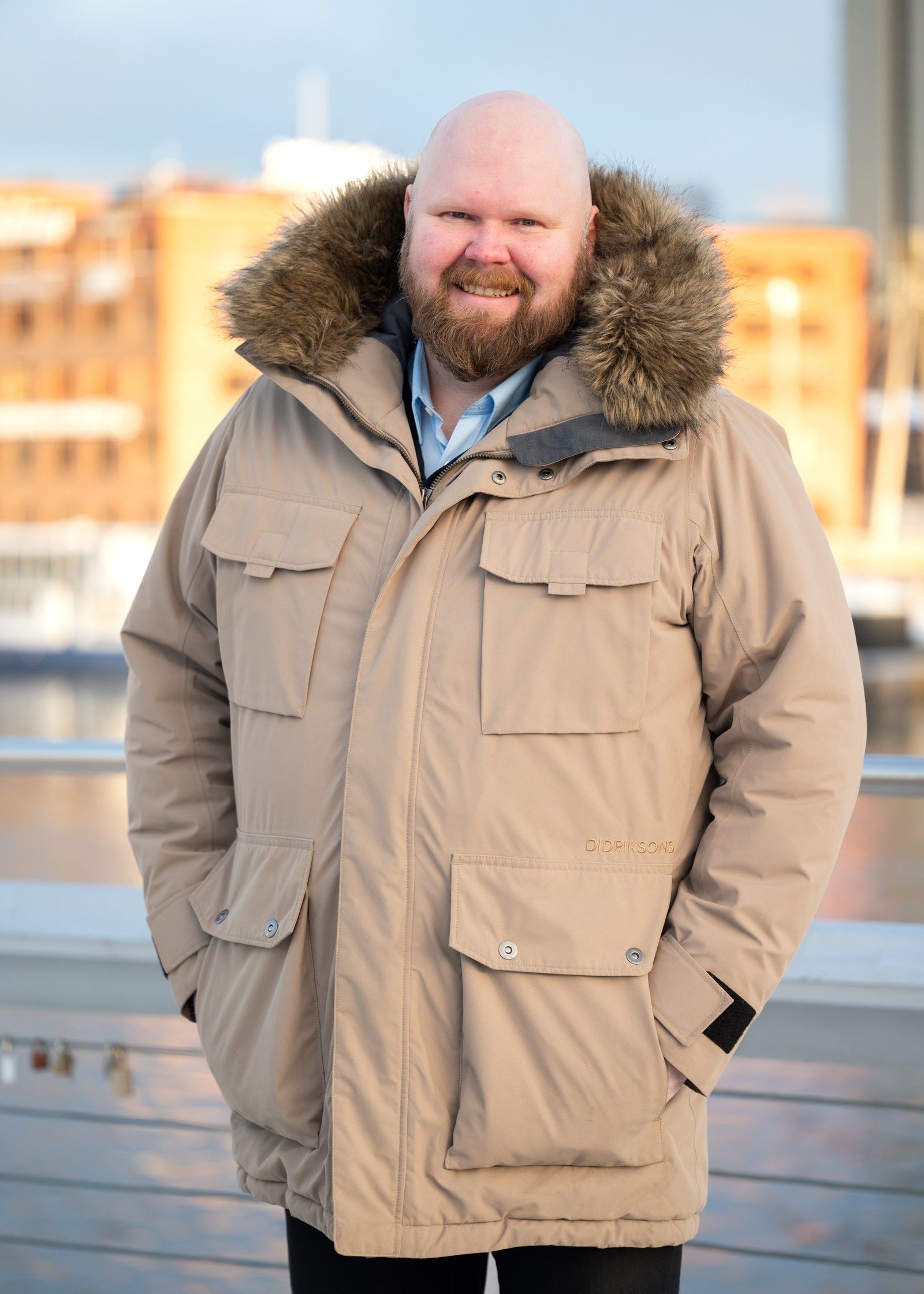 Antti Brunni in a winter coat on a city waterfront, brick buildings behind him.