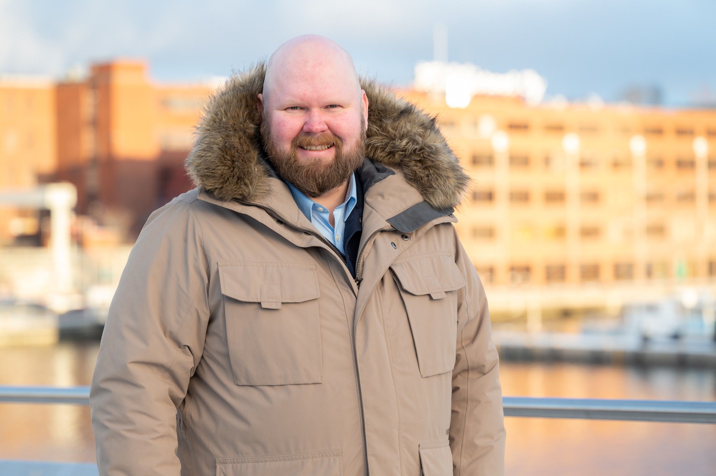Antti Brunni in a winter coat on a city waterfront in afternoon light.