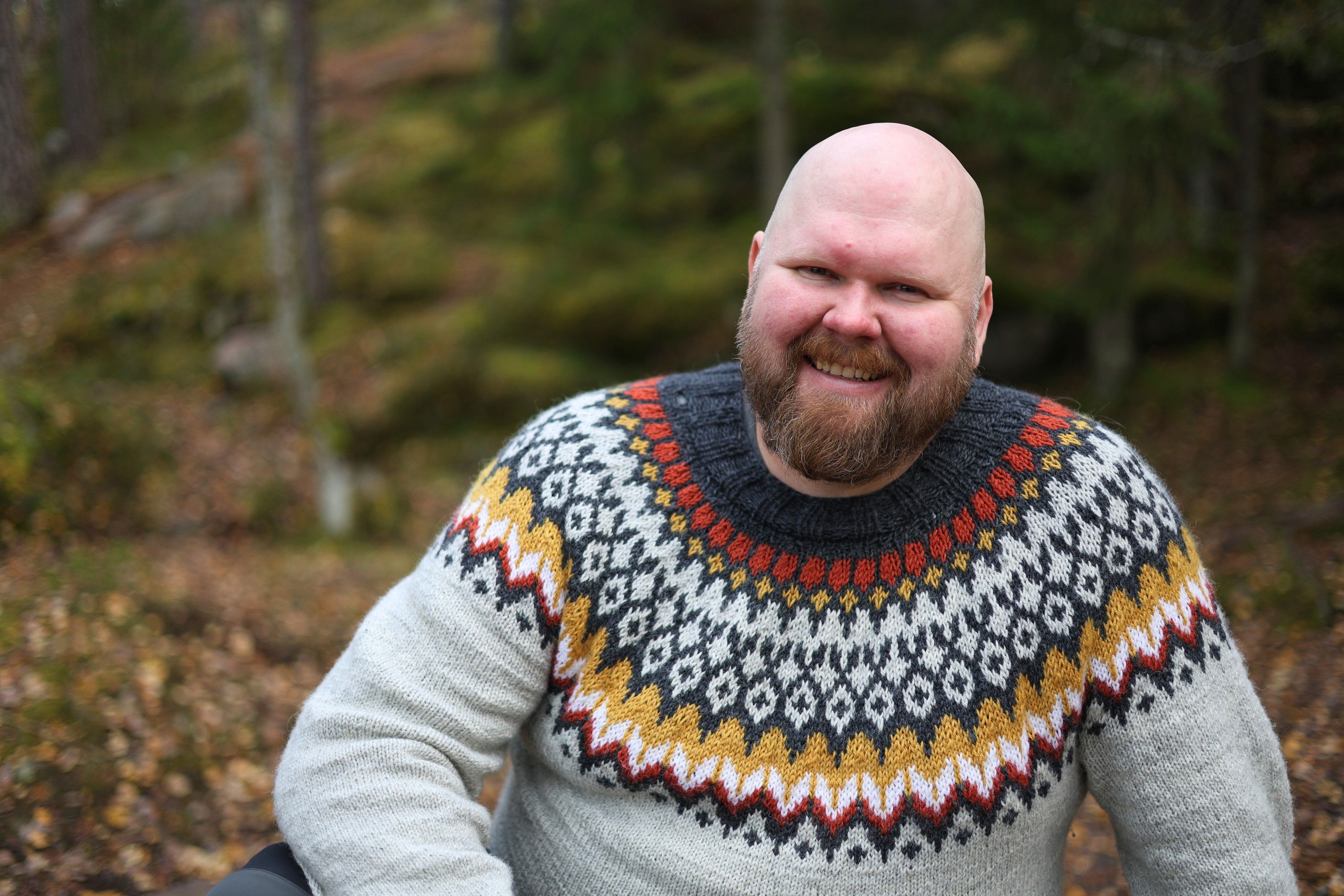 Antti Brunni smiling in a wool sweater in an autumn forest.